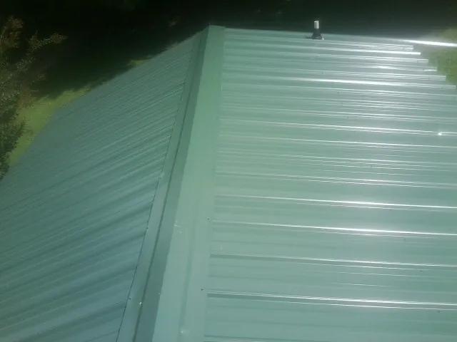 New green metal panels meeting at the ridge of a roof — Flat Roof Repair work by our crew in Williamsburg